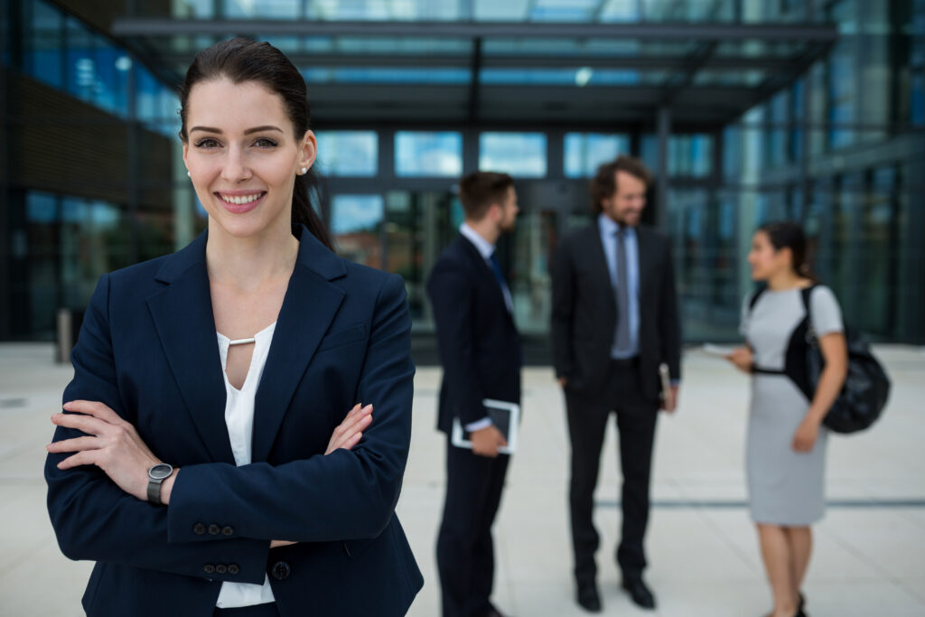 A confident business professional standing outside an office with her colleagues in the background